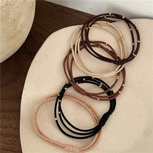 Detailed view of elastic hair ties with gold beads in neutral earth tones on a tray