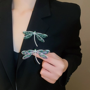 Detail van libellenbroches met groene en paarse zirkonen op de revers van een blazer