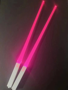 Close-up of two pink LED lightsaber chopsticks glowing in the dark with white handles