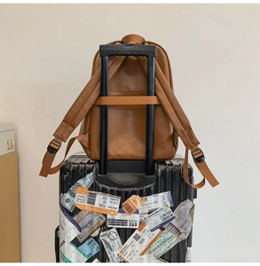 Brown faux leather backpack with luggage strap fixed on suitcase handle for travel