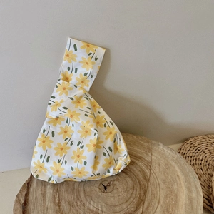 Detail of floral cotton wrist bag with yellow daisy pattern on rustic wood base