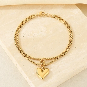 Detail of gold double-layer chain bracelet with heart pendant on stone surface