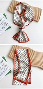 Detail of silk scarf with black D pattern, orange trim, displayed on a wooden tray
