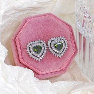 Close-up of heart-shaped dark green zircon earrings displayed on a pink velvet jewelry box