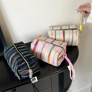Detail of colorful striped woven makeup bags in black, pink, and beige with zippers