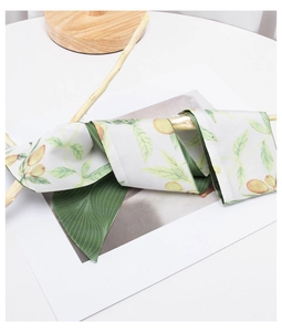 Close-up of silk-textured ribbon scarf in green, white, and ginger yellow on white background