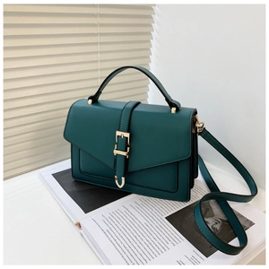 Detail of dark green crossbody bag with gold buckle on a magazine background