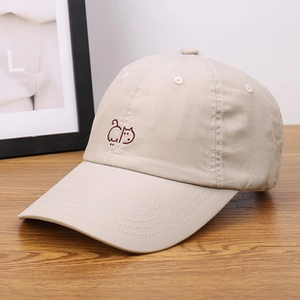 Close-up of beige teddy fleece baseball cap with minimalist embroidered cat on wooden table