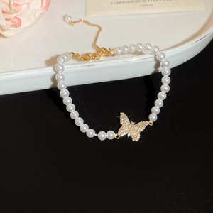 Detail of 18k gold plated pearl bracelet with butterfly charm on elegant white plate