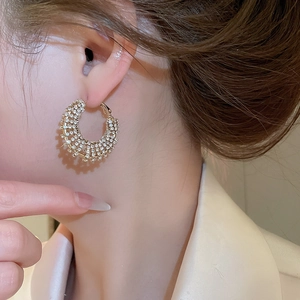 Close-up of model wearing gold-plated hoop earrings with shimmering white rhinestones