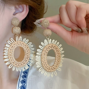Détail de boucles d'oreilles bohèmes en raphia tressé avec franges en paille beige