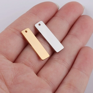 Close-up of small gold and silver stainless steel rectangle pendants held in hand