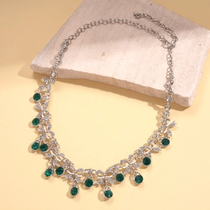 Close-up of silver palace style necklace with green crystals and teardrop pendant on stone
