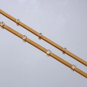 Close-up of golden flat blade chains with square clear zircon stones on a grey surface