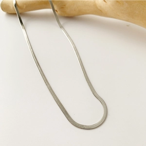 Close-up of a silver herringbone snake chain necklace draped on a wooden stand