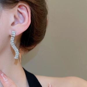 Detail of silver S-shaped wave earrings with shimmering rhinestones on a model