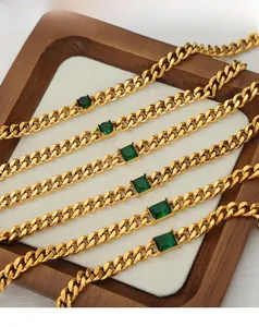 Detail of gold-plated Cuban chain bracelets with inlaid green zircon on wooden tray
