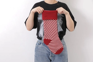 Close-up of a person holding a red and white diagonal striped knitted Christmas stocking