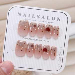 Pink gradient press-on nails with red hearts and polka dots on a display card