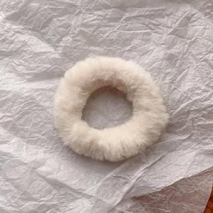 Close-up of soft beige faux rabbit fur scrunchie on textured paper background