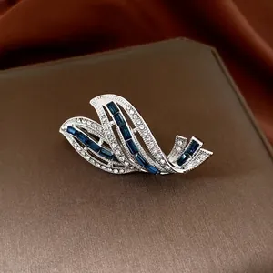 Elegant silver feather brooch with blue gems and crystals on luxury brown leather background