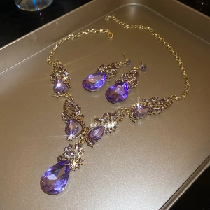 Close-up of luxury gold necklace and earrings set with purple teardrop crystals