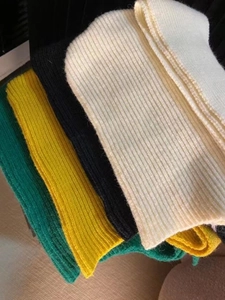 Detail of ribbed knit texture on folded scarves in cream, black, yellow, and green colors
