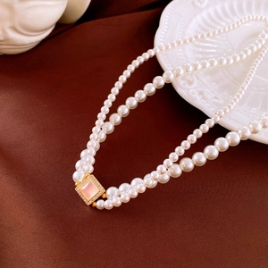 Detail of a vintage double-layer pearl necklace with a pink square pendant on white porcelain