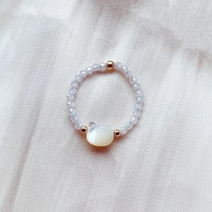 Macro detail of a beaded ring with grey faceted beads and a white shell cat charm