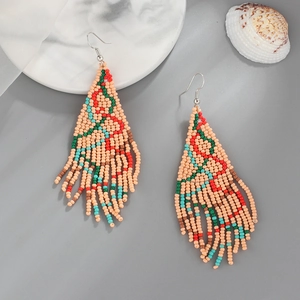 Handmade boho tassel earrings with beaded Christmas tree design on marble surface