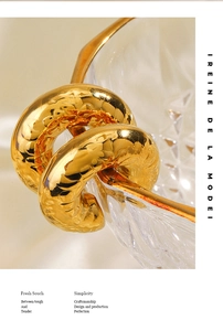 Detailed macro view of 18K gold-plated chunky twisted knot hoop earrings on a glass edge