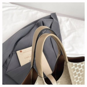 Detail of monogram tote bag with leather handles on a minimalist background
