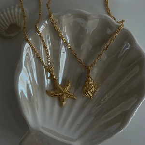Close-up of golden starfish and shell necklaces on a white shell-shaped ceramic dish