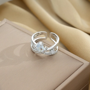 Macro detail of silver multilayer crossover ring with teardrop zircon on silk background