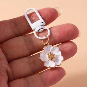 Handheld view of a white enamel flower keychain with gold edges and metallic lobster clasp