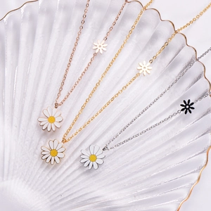 Three dainty daisy pendant necklaces in gold, rose gold and silver on a shell tray