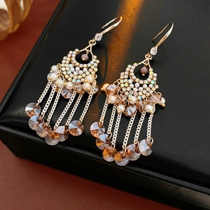 Detail of gold tassel earrings featuring faceted crystal beads and pearls on black leather