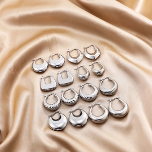 Polished stainless steel silver hoop earrings set on beige silk fabric background