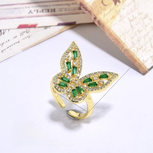 Macro detail of gold-plated butterfly ring featuring green zircons on a vintage letter background