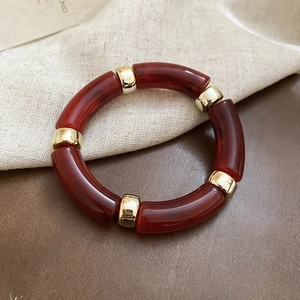 Detail of dark red iridescent acrylic tube beads with gold metal spacers on a beige linen surface