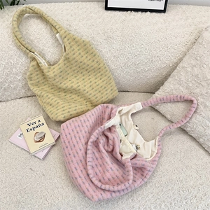Macro shot of knitted plush tote bags in pale yellow and pink on a textured sofa