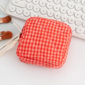 Detail of red checkered quilted makeup bag with ribbon zipper pull on white desk