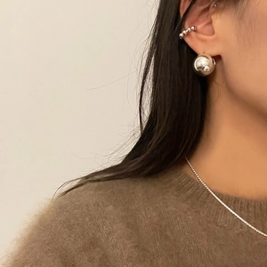Detail of model wearing large silver spherical stud earrings and a beaded ear cuff