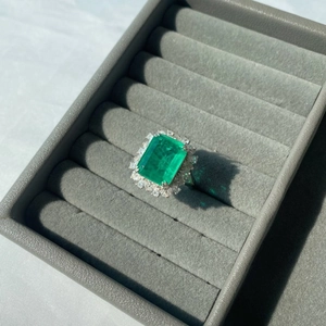 Macro shot of emerald-cut green gemstone ring with halo diamonds in a gray velvet box