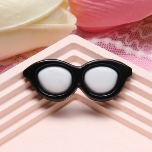 Miniature black resin sunglasses charm for DIY crafts on a decorative pink stand