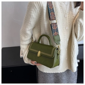 Detail of dark green PU leather bag with golden oval lock and ethnic woven strap