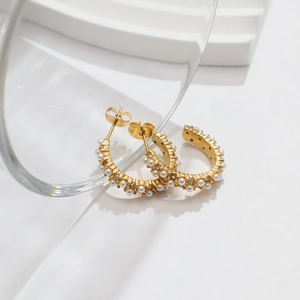 Close-up of 18k gold-plated C-shaped earrings with zircon and pearl embellishments