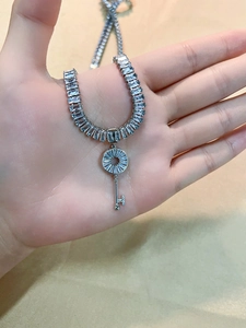 Detailed close-up of a silver key pendant with baguette-cut zircons on a tennis chain