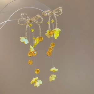 Detail of handcrafted gold butterfly bow earrings with yellow beaded flowers and tassels