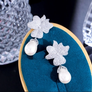 Macro detail of zircon flower earrings with teardrop pearls on blue velvet background